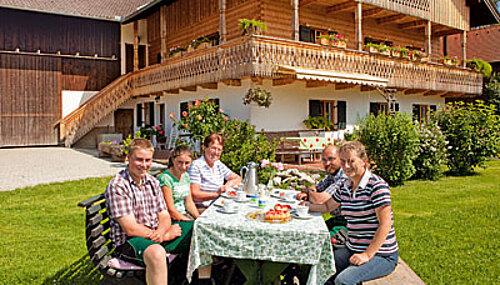 Familie am Tisch sitzend vor dem Wohnhaus